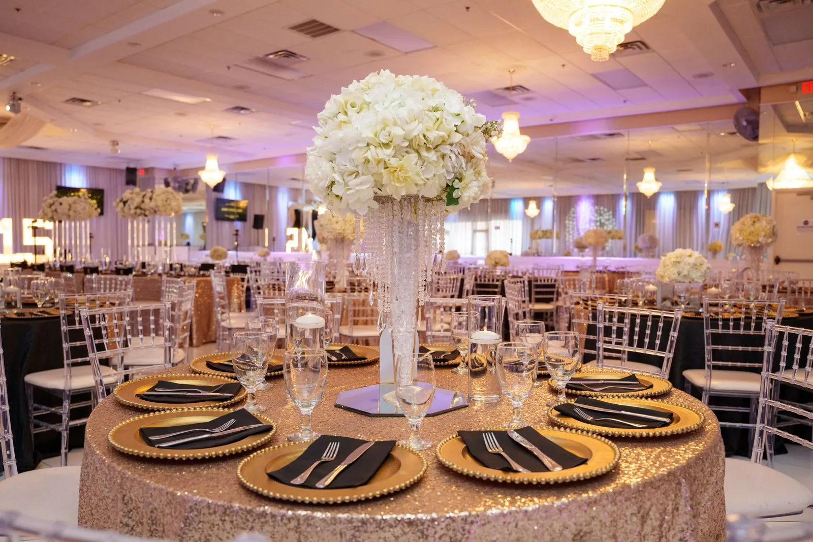 A reception table in gold and black with a white floral centerpiece at Luxor Banquet Hall