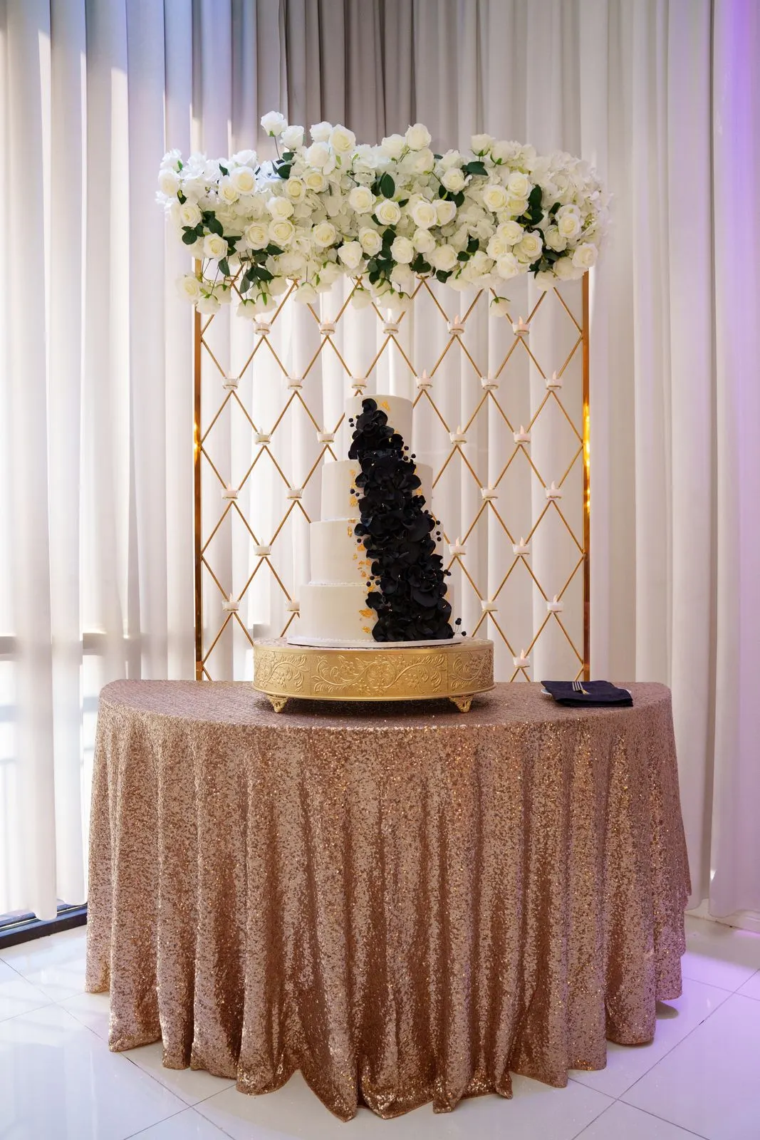 Un pastel de quinceañera de cuatro pisos en blanco con flores negras en cascada en Luxor Banquet Hall
