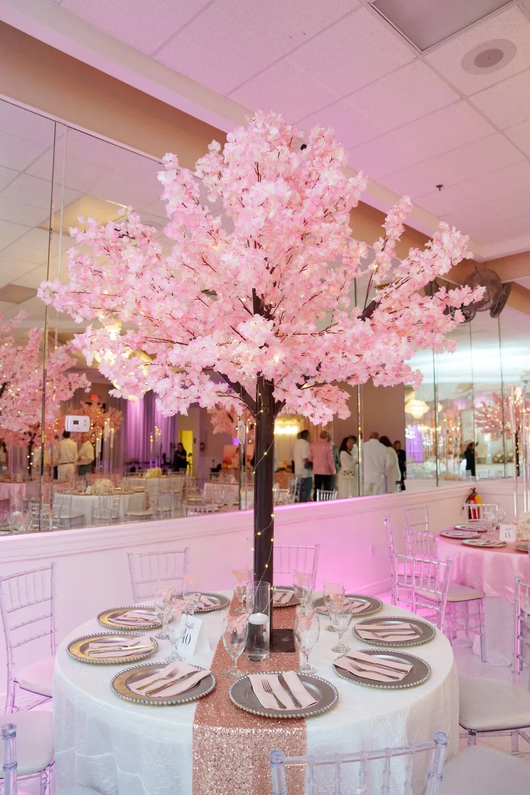 A reception table at Luxor Banquet Hall set with chargers and glassware under a cherry-blossom centerpiece